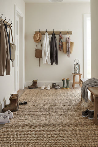 Entryway with shoes, coats, and bags on hooks and a woven rug.